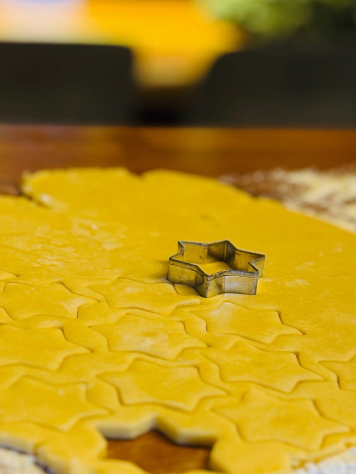Sternförmiger Ausstecher steckt in ausgerolltem, gelbem Keksteig.