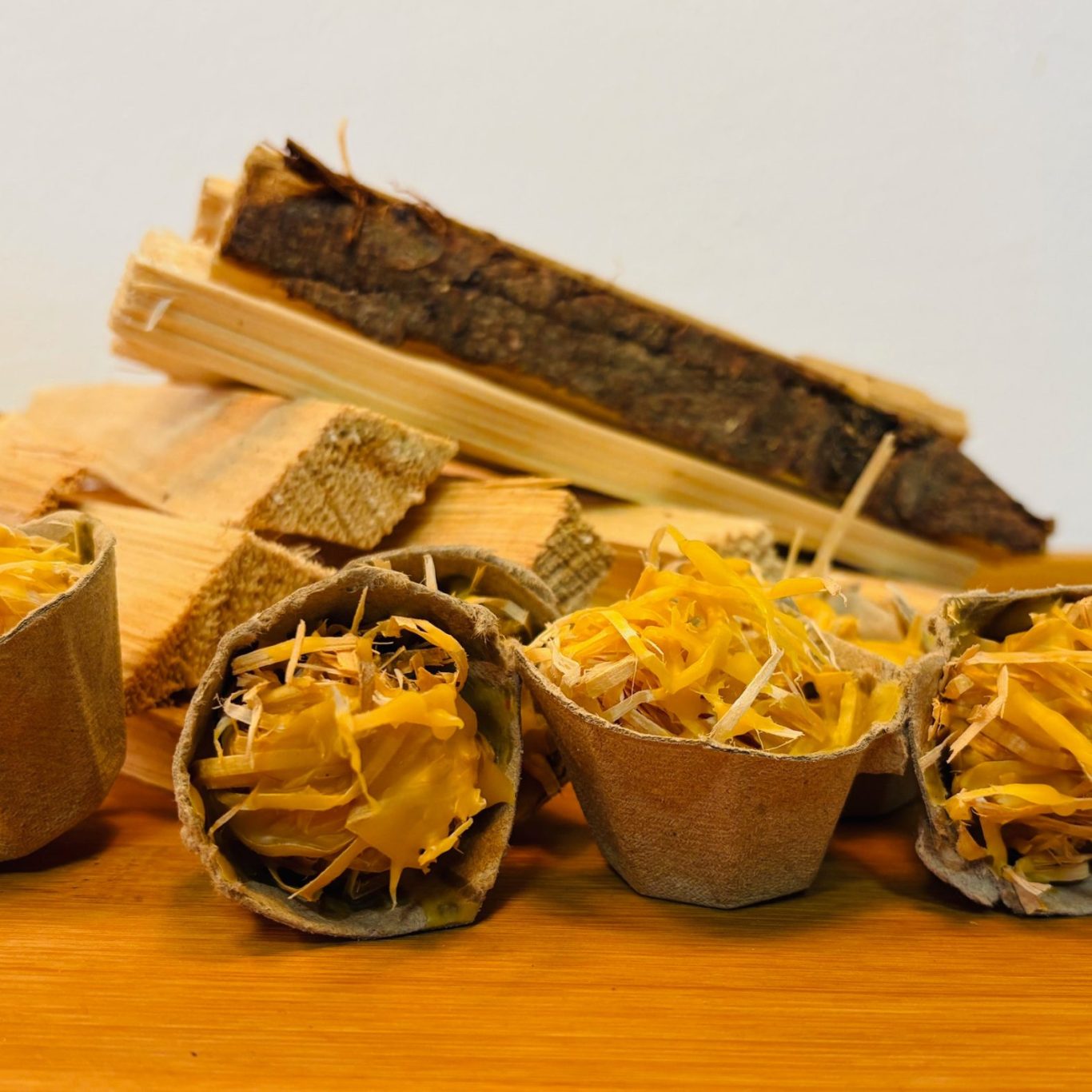 Drei kleine Pappbecher mit gefüllten Teigstücken und Käse, daneben Holzscheite.