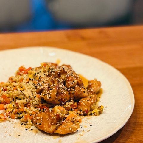 Ein Teller mit platzierten Hähnchenstücken und buntem Gemüse, garniert mit Sesam.