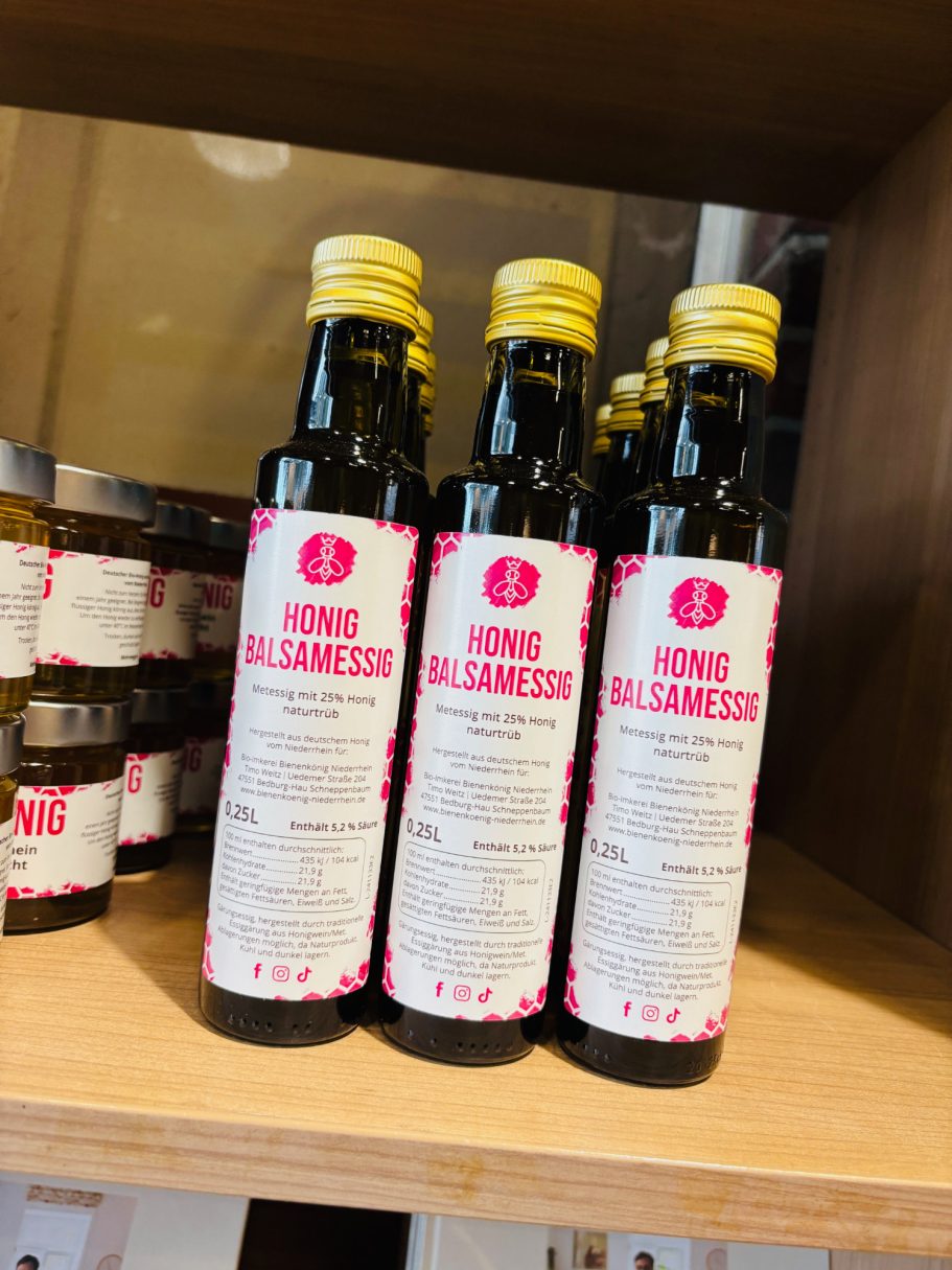 Drei Flaschen mit Olivenöl auf einem Holztisch, mit pinken Etiketten.