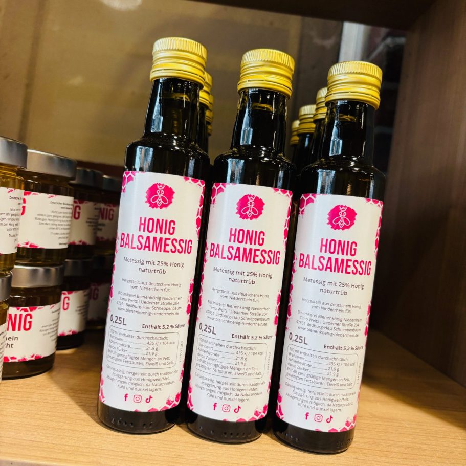 Drei Flaschen Honig-Essig auf einem Regal, etikettiert mit rosa Schrift.