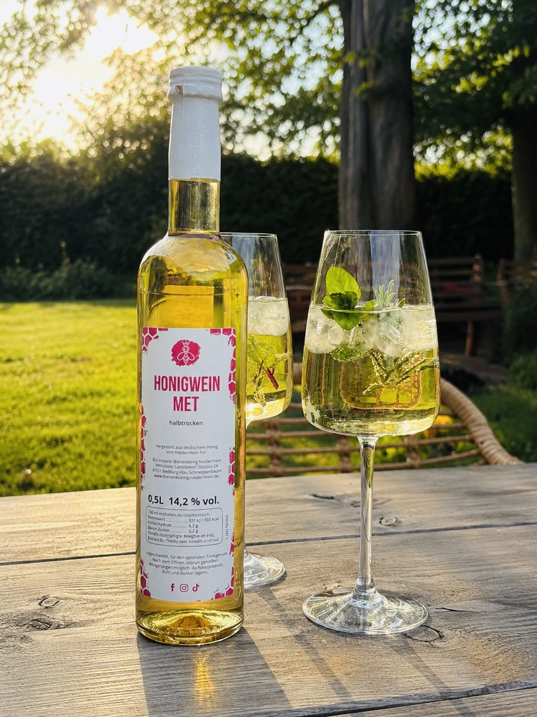 Flasche Weißwein mit zwei Gläsern, gefüllt mit Getränk und Minzblättern, im Garten.