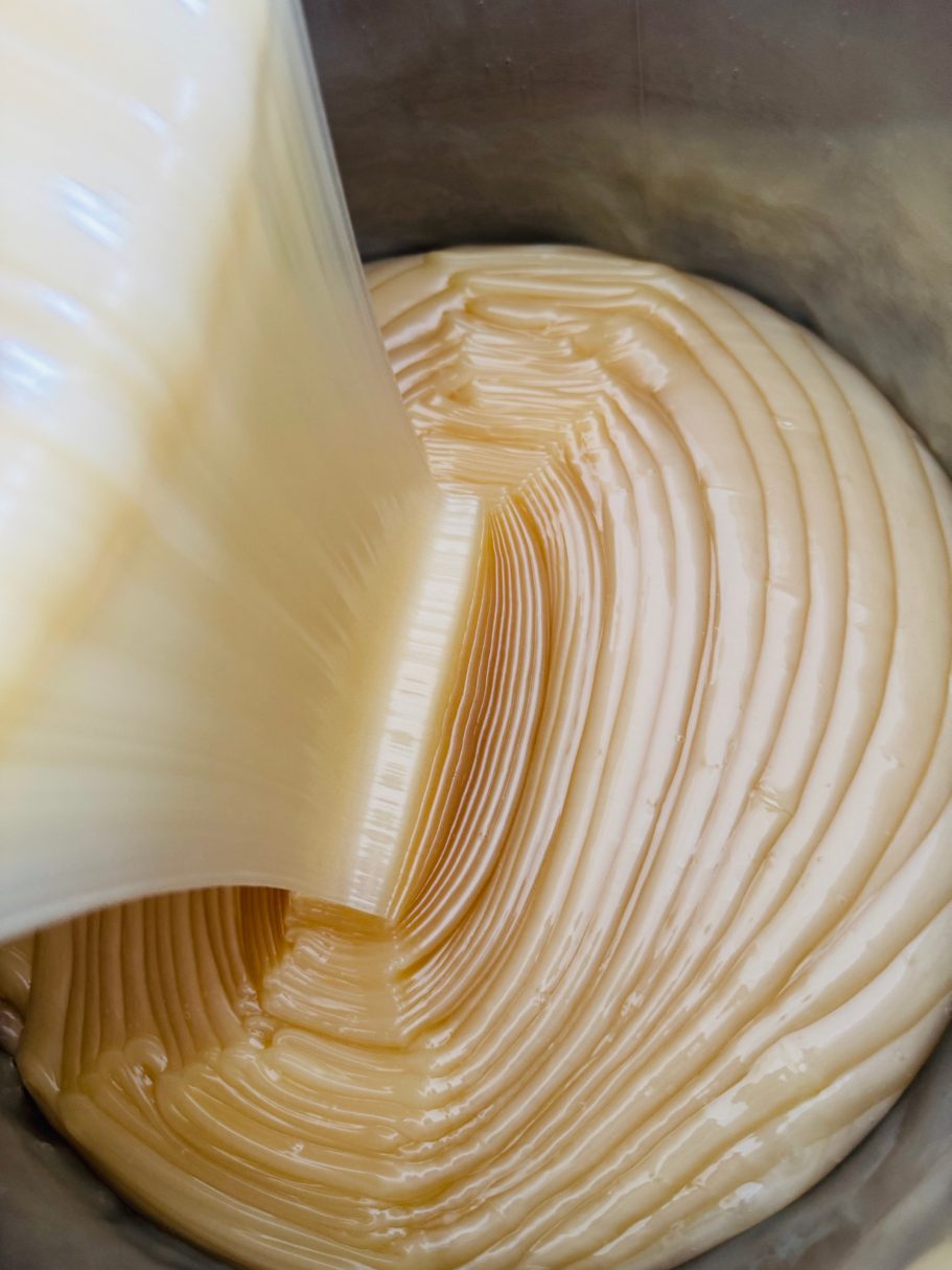 Zähflüssige, glatte Creme fließt in eine runde Schüssel mit spiralförmigem Muster.