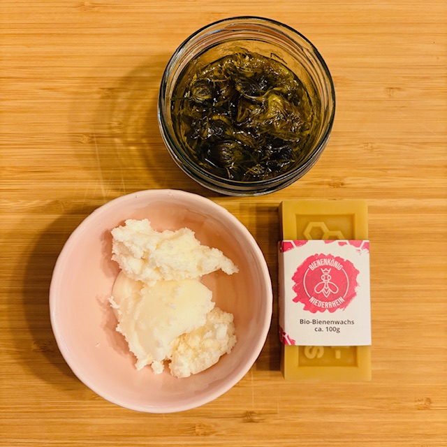 Schüssel mit Creme, Glas mit unkenntlichem Inhalt und Seife auf Holzuntergrund.