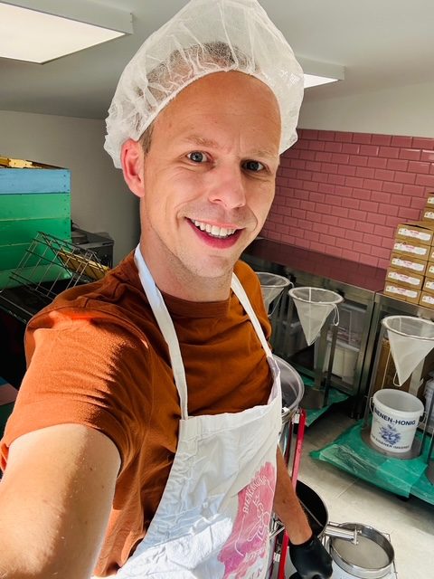 Lächelnder Mann in Kochuniform mit Schürze in einer Küchenumgebung.