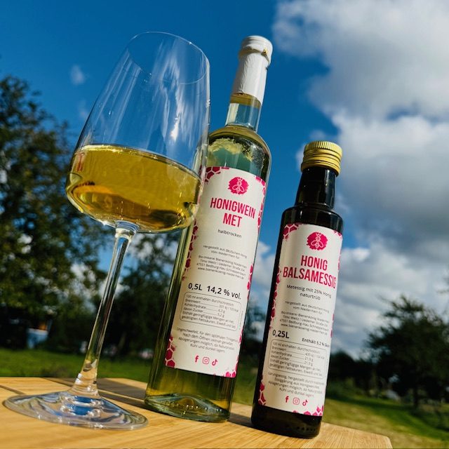 Honigweinin einem Glas neben einer Flasche und Essig, unter blauem Himmel.