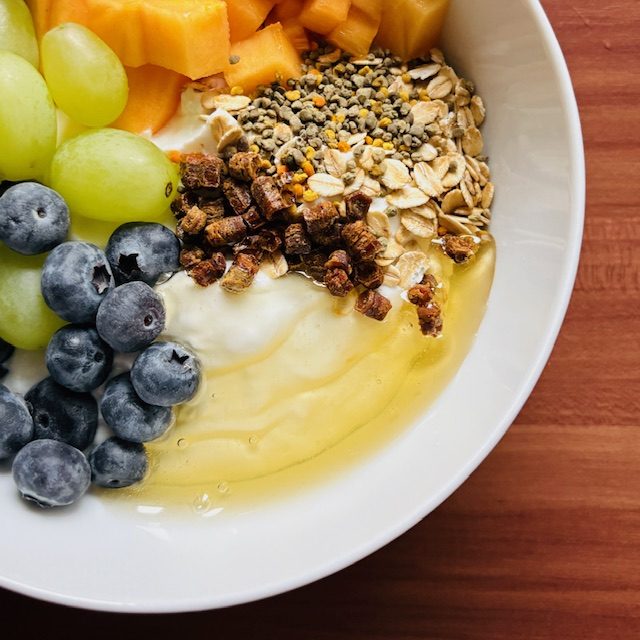 Schüssel mit Joghurt, frischen Früchten, Haferflocken und Honig.