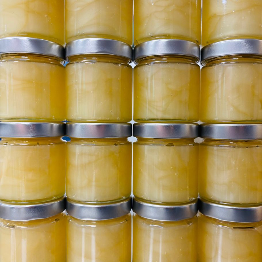 Reihe von Einmachgläsern mit gelbem Inhalt und metallischen Deckeln.