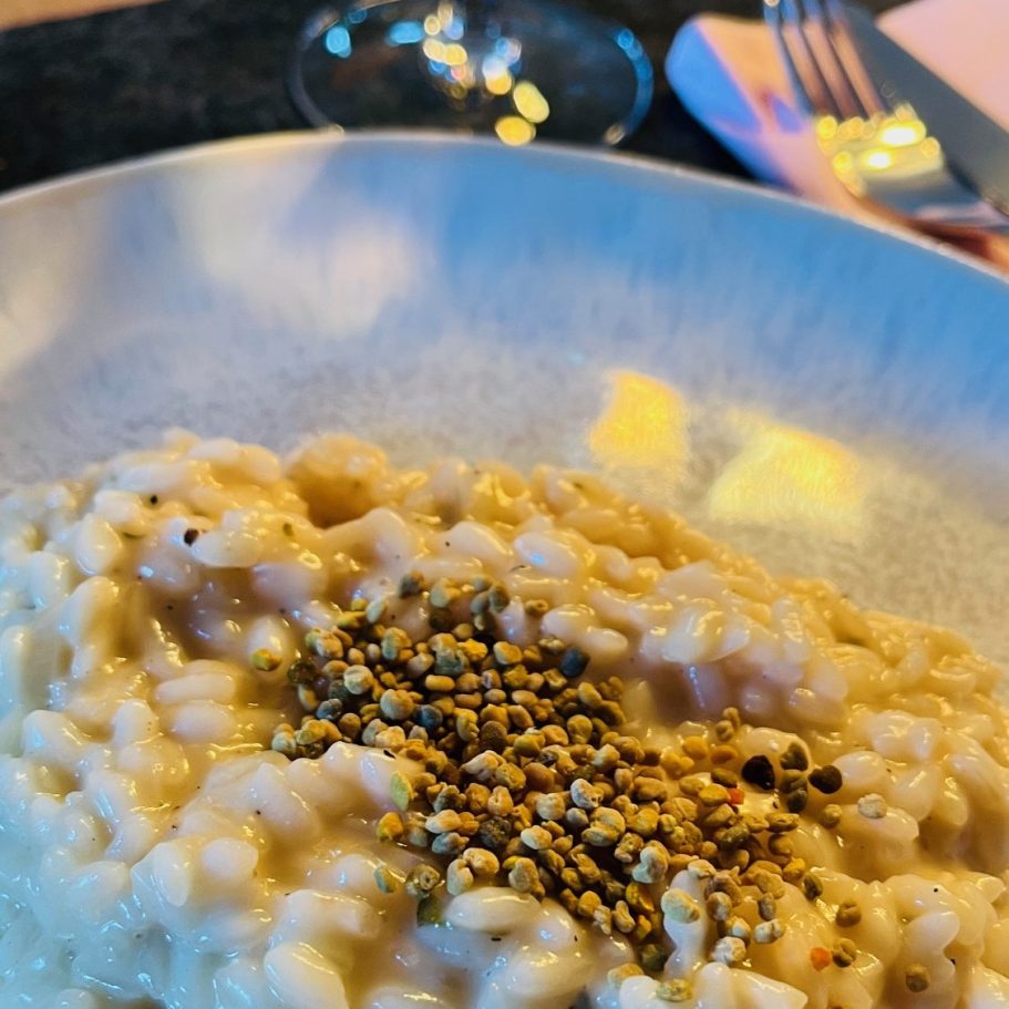 Cremiges Risotto mit Gewürzen auf einem eleganten Teller. Gläser und Besteck im Hintergrund.