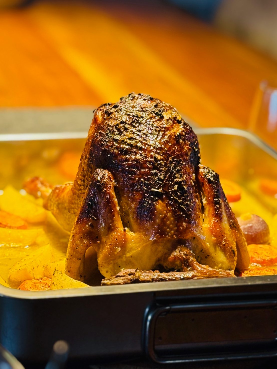Geröstetes Hähnchen in einer Bratpfanne mit Gemüse umgeben auf einem Holztisch.