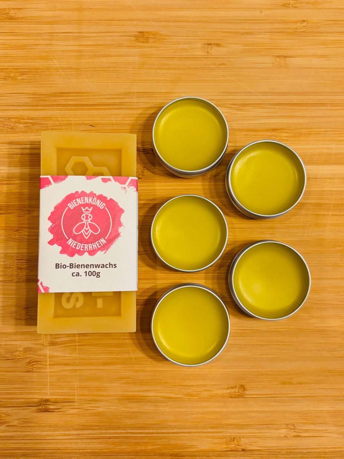 Fünf Behälter mit grünem Balsam und einer Verpackung auf Holzuntergrund.