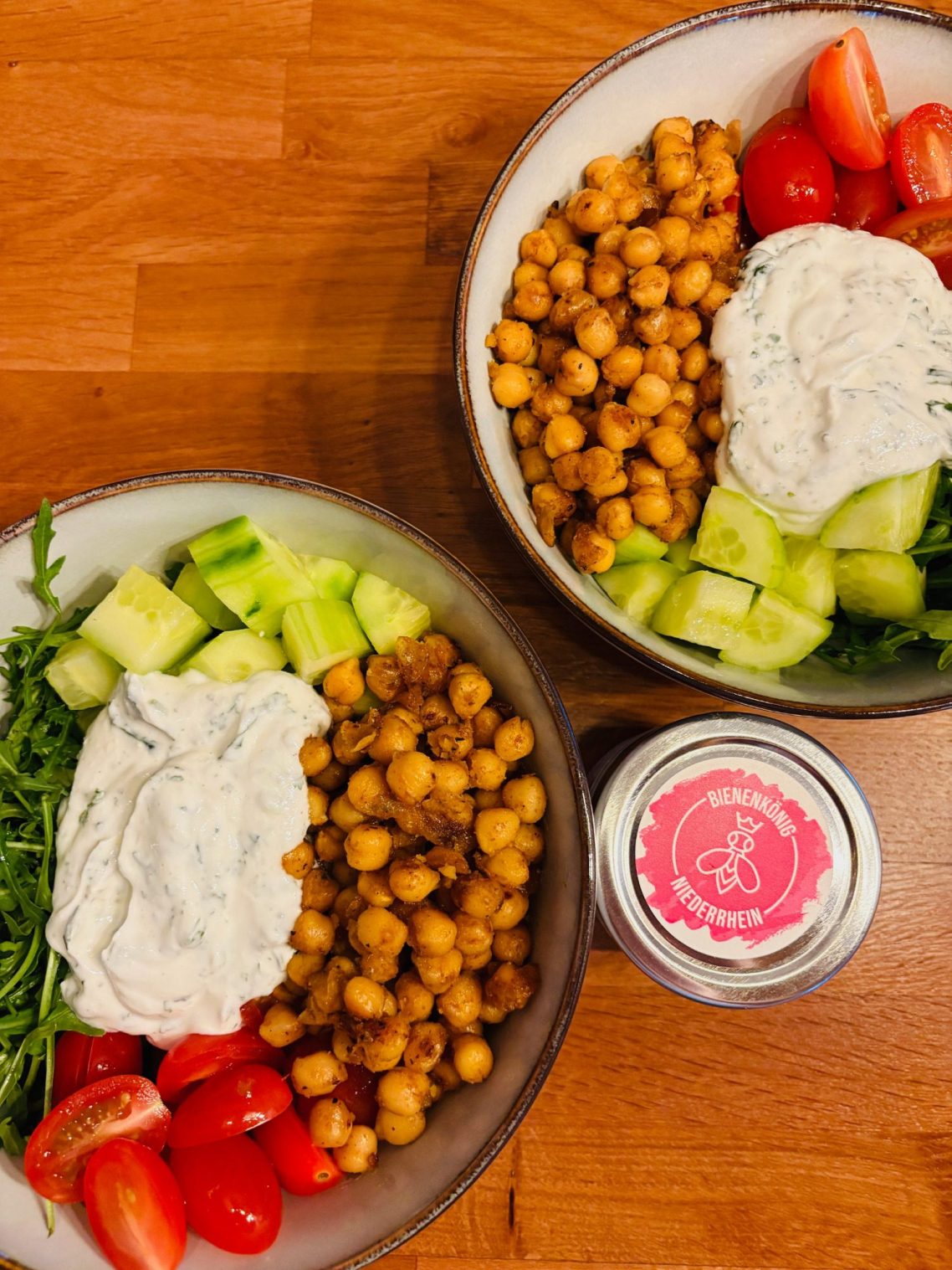 Zwei Schalen mit Kichererbsen, Gurken, Tomaten, Joghurt-Dip und frischem Salat.