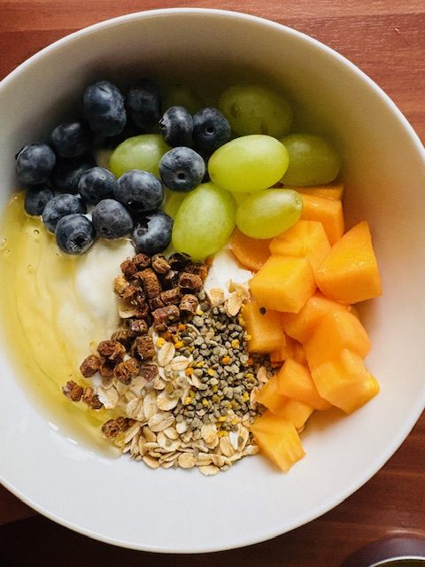 Schale mit Joghurt, Müsli, Heidelbeeren, Trauben und gewürfelter Mango.