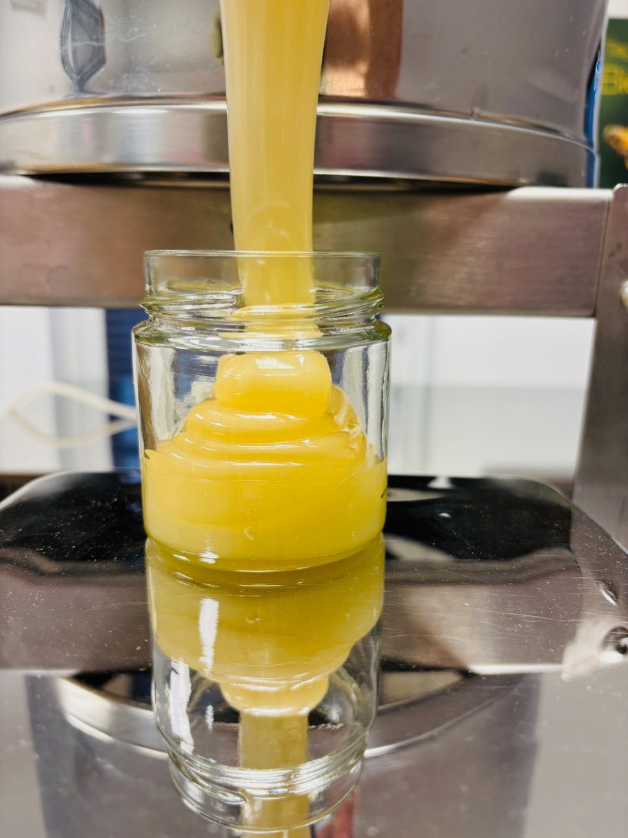 Honig läuft aus einem Behälter in ein Glas und bildet dabei eine goldene, glänzende Schicht.