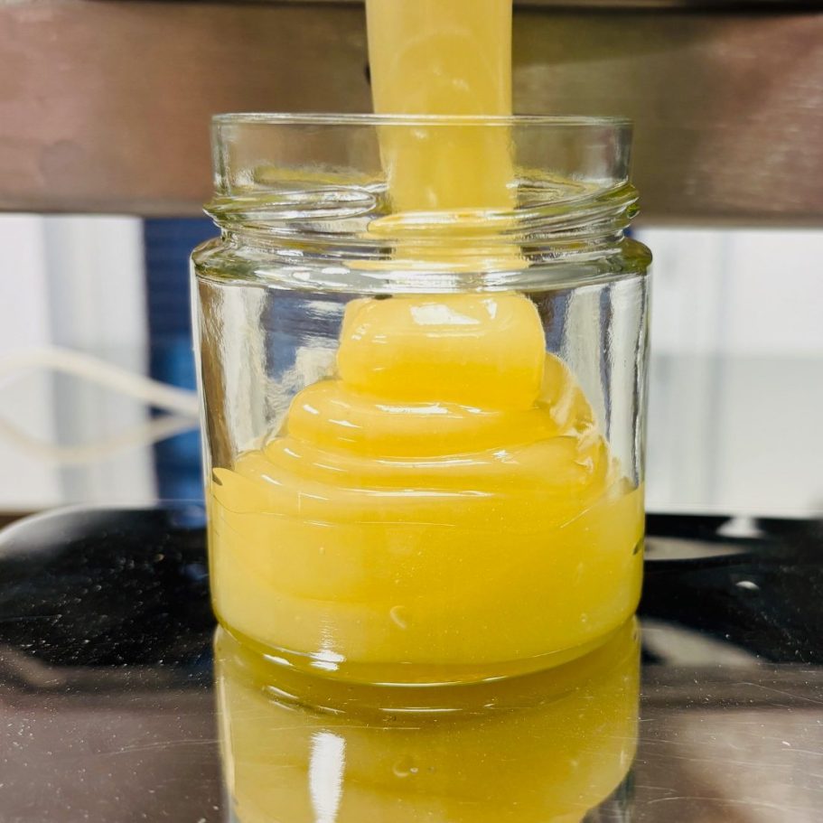 Ein Glas mit honiggelber, zähflüssiger Substanz, die hineinläuft.