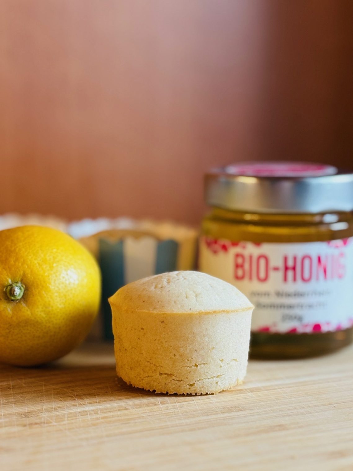 Eine Zitrone, ein Muffin und ein Glas Bio-Honig auf einem Holzuntergrund.