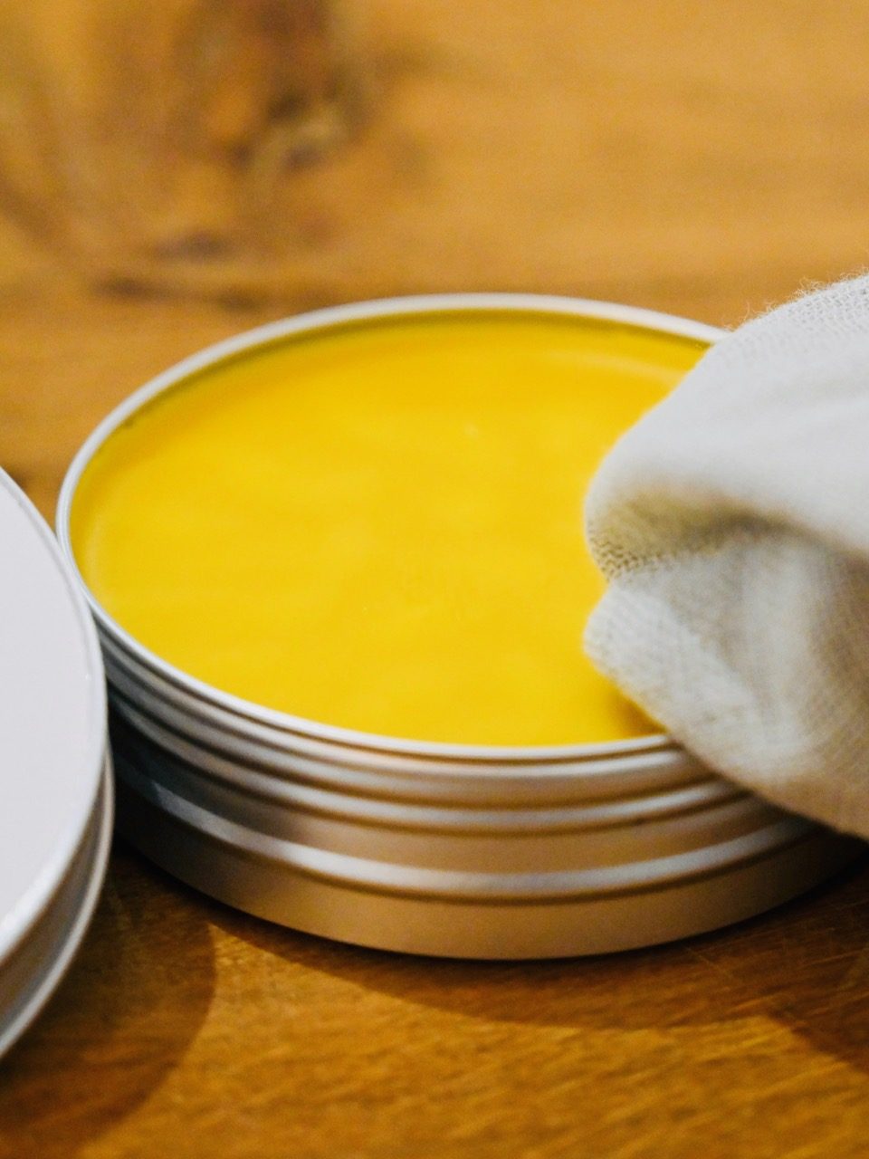 Gelbe Pflegecreme in einer Dose, teilweise mit einem Tuch berührt.